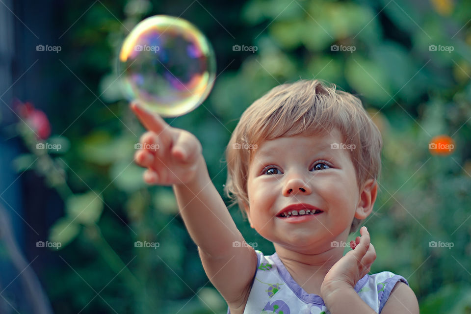 Happy smiling little girl is playing with soap bubble