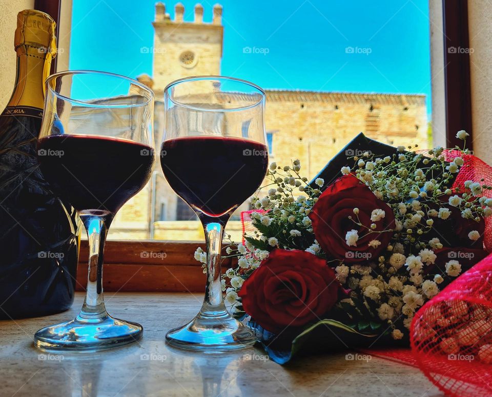 glasses of wine and a bouquet of roses in front of an open window