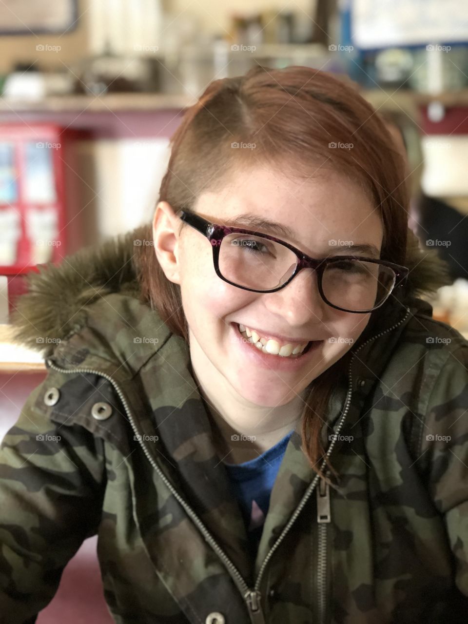 Smiling teenage girl wearing glasses, camouflage coat with fur and shaved haircut