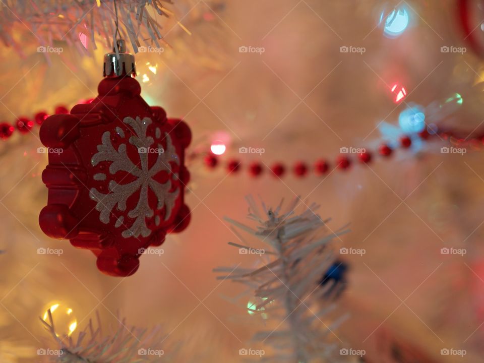 A red star ornament with white glitter hangs on a white Christmas tree with a soft glow from the lights. 
