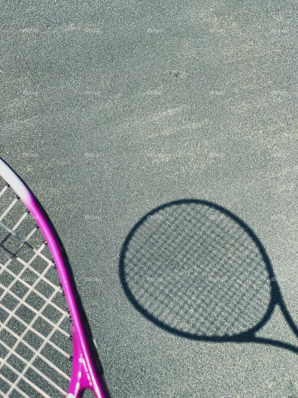Purplish pink tennis racket and its shadow on clay courts.