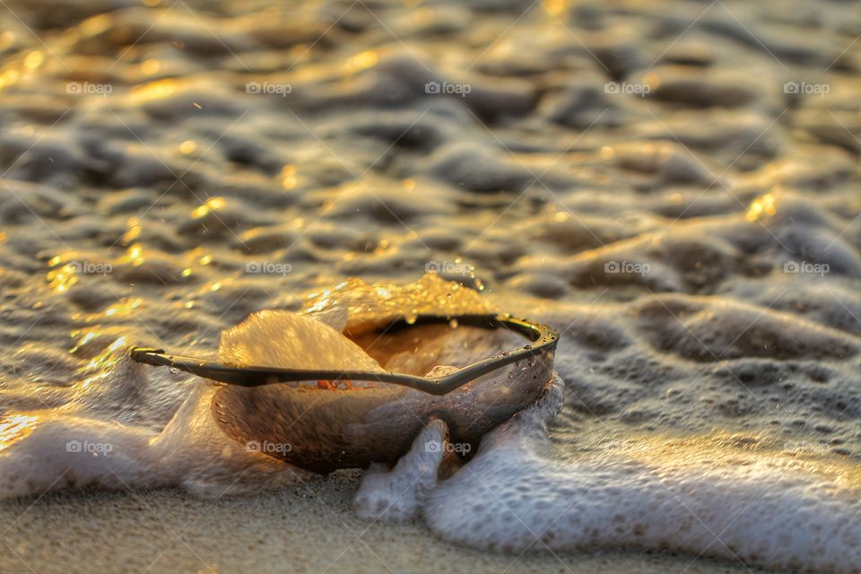 sunglasses under foam in the beach at sunrise