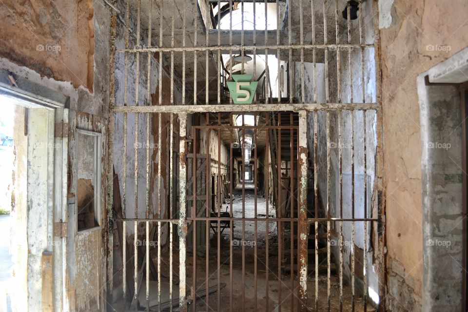 A view of an abandoned prison corridor with an arched ceiling through rusty metal bars