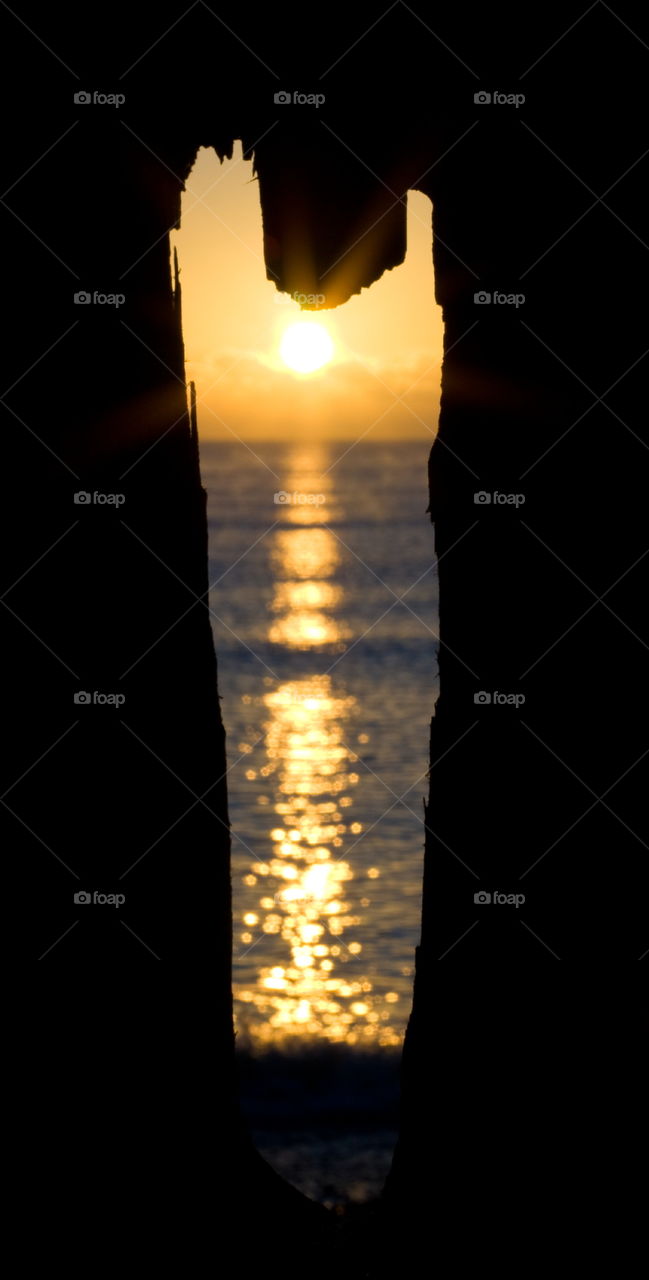 A blurry sunrise over the sea can be seen through a crack in the wooden groyne - Winchelsea UK 