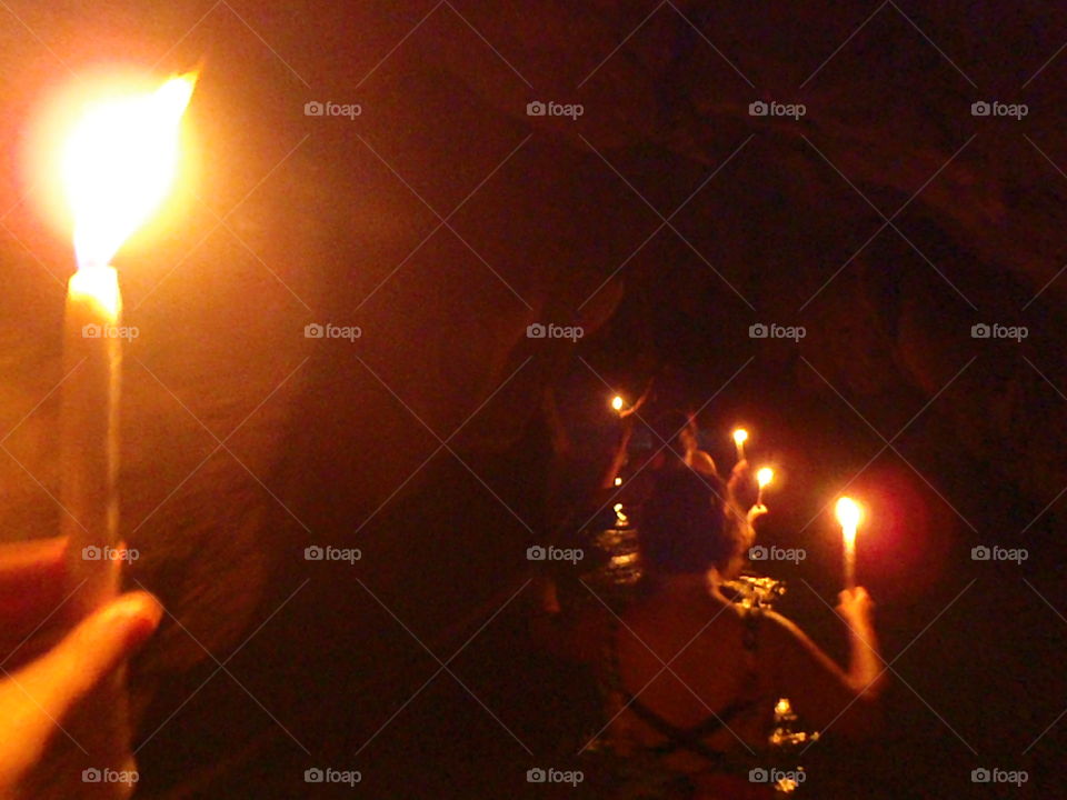 Cave tour by candle light. Line of brave tourist in cave holding their candles in waist deep river