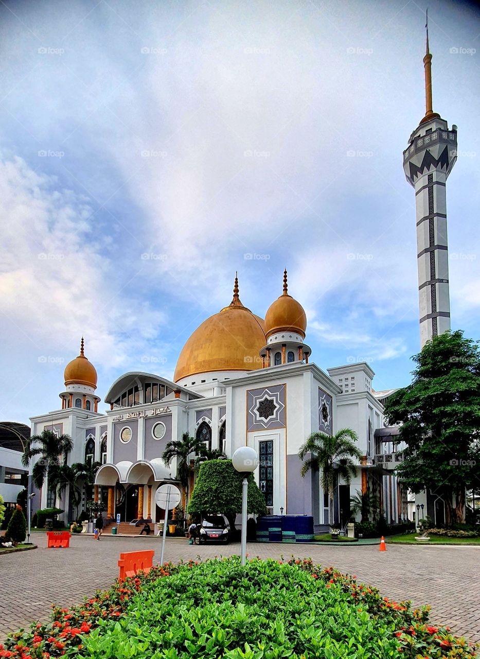 A mosque with a golden dome surrounded by tress is in the city of Surabaya,Indonesia