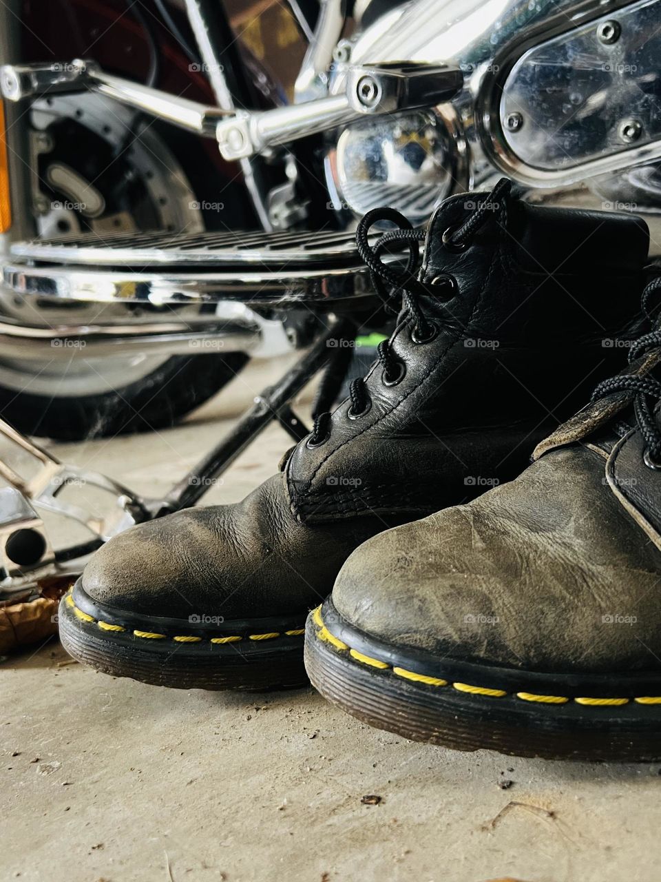 Closeup of worn, older Doc Marten classic boots with motorcycle in background 