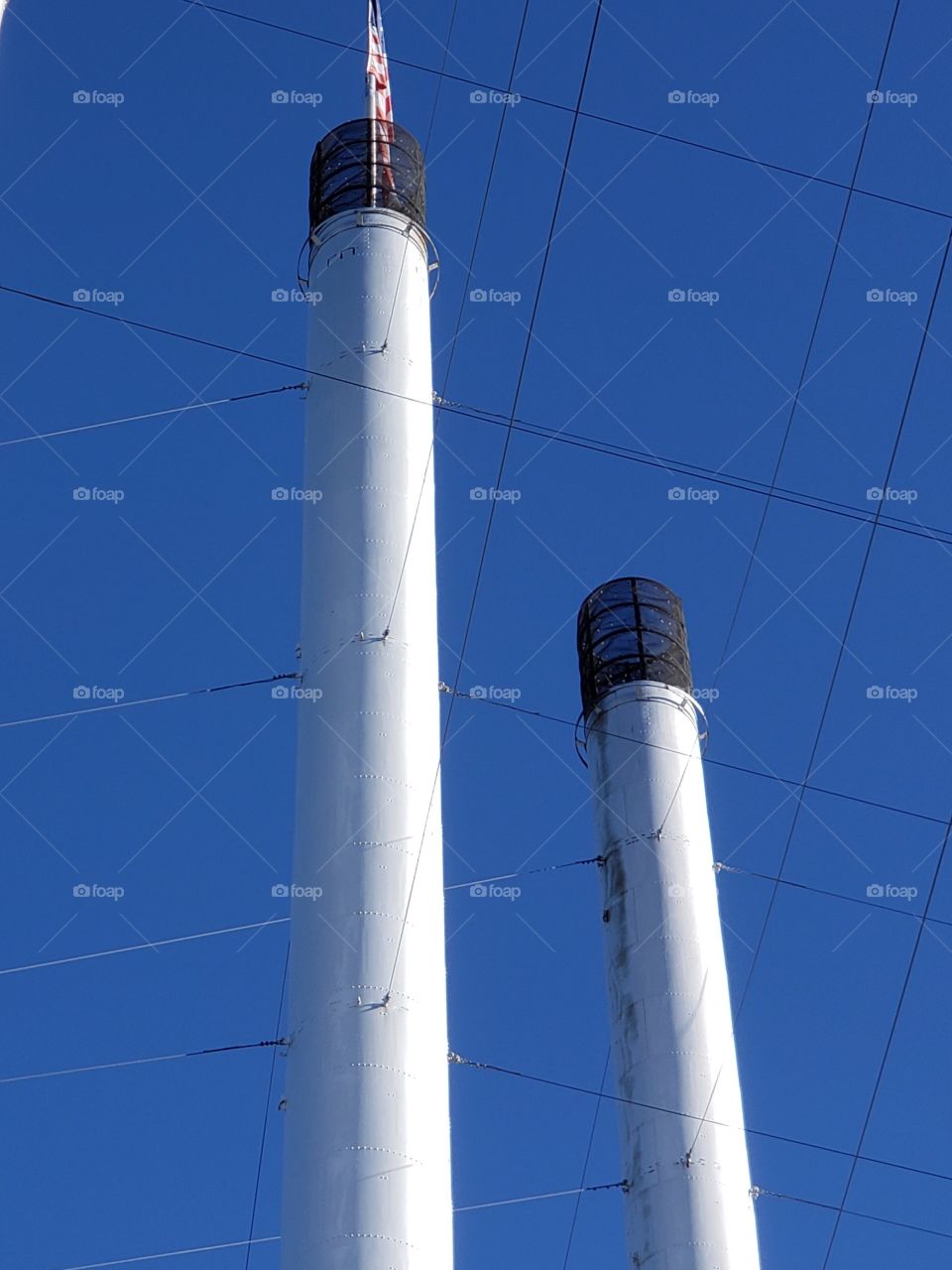 Old smoke stacks from an Oregon Mill no longer in use with an American flag mounted at the top against clear blue skies on a fall morning. 