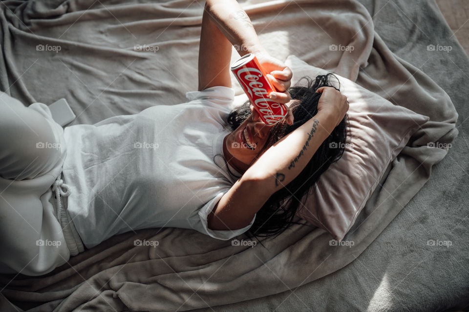 the girl lies on the bed and holds a Coca Cola