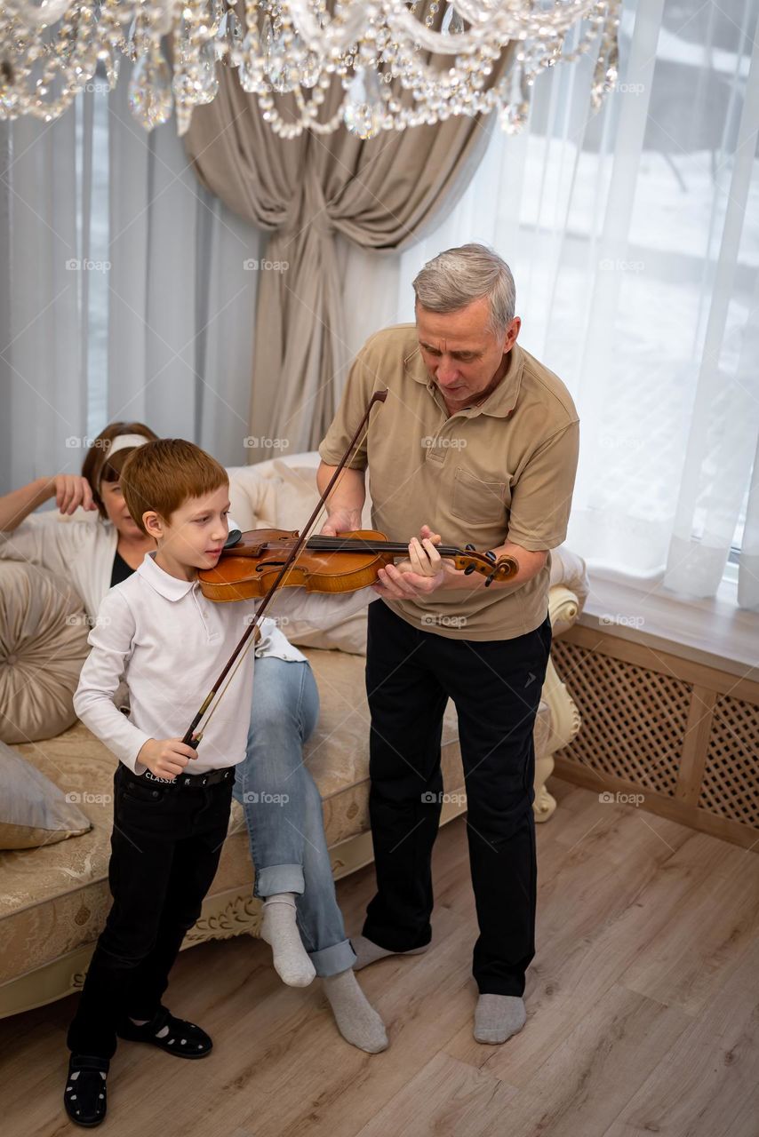 Red-haired boy plays the violin in a bright room, the family listens to music
