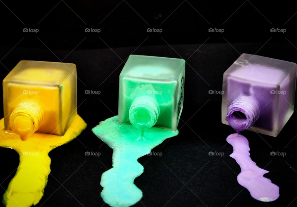 Three vials of flow out nail polish leaking: purple, yellow and green. Black background
