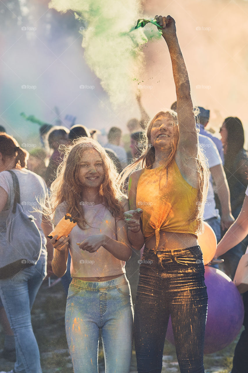 Portrait of happy smiling young girls with colorful paints on faces and clothes. Two friends spending time on holi color festival. Real people, authentic situations