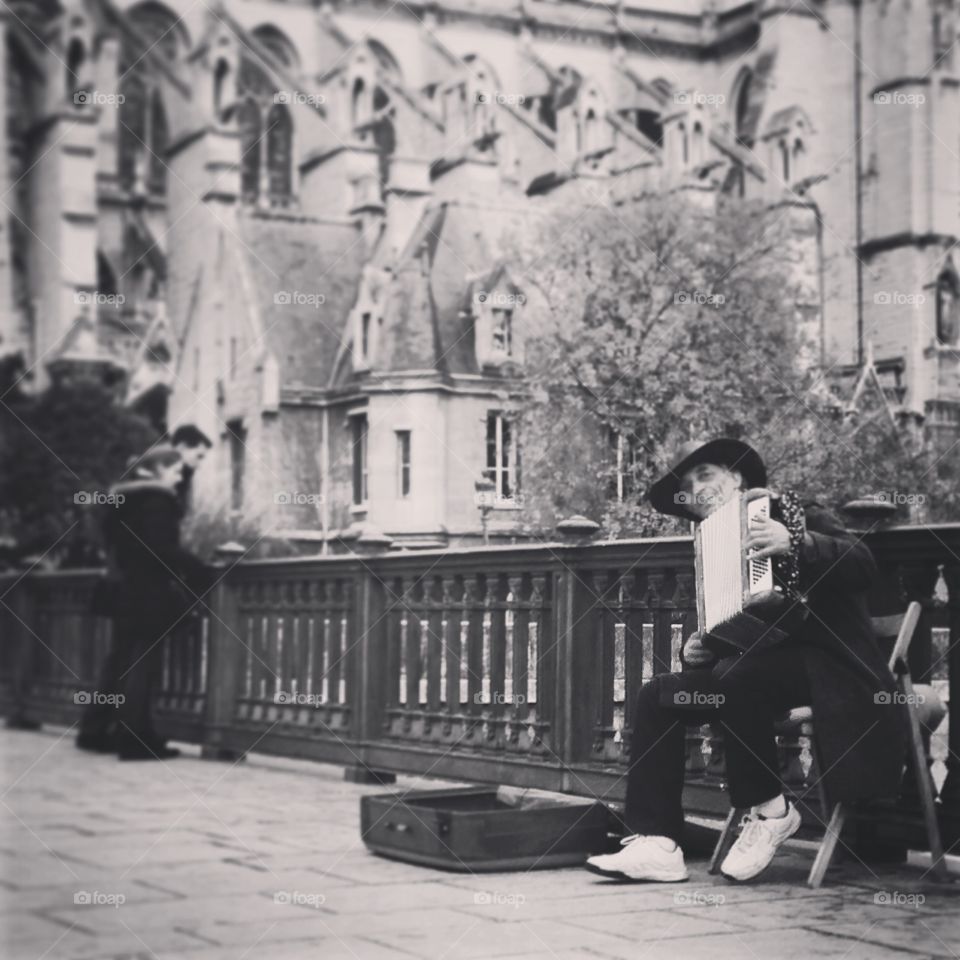 Notre Dame Street Performer. A man plays the accordion outside the Notre Dame Cathedral in Paris. A couple stops to enjoy the music in the background