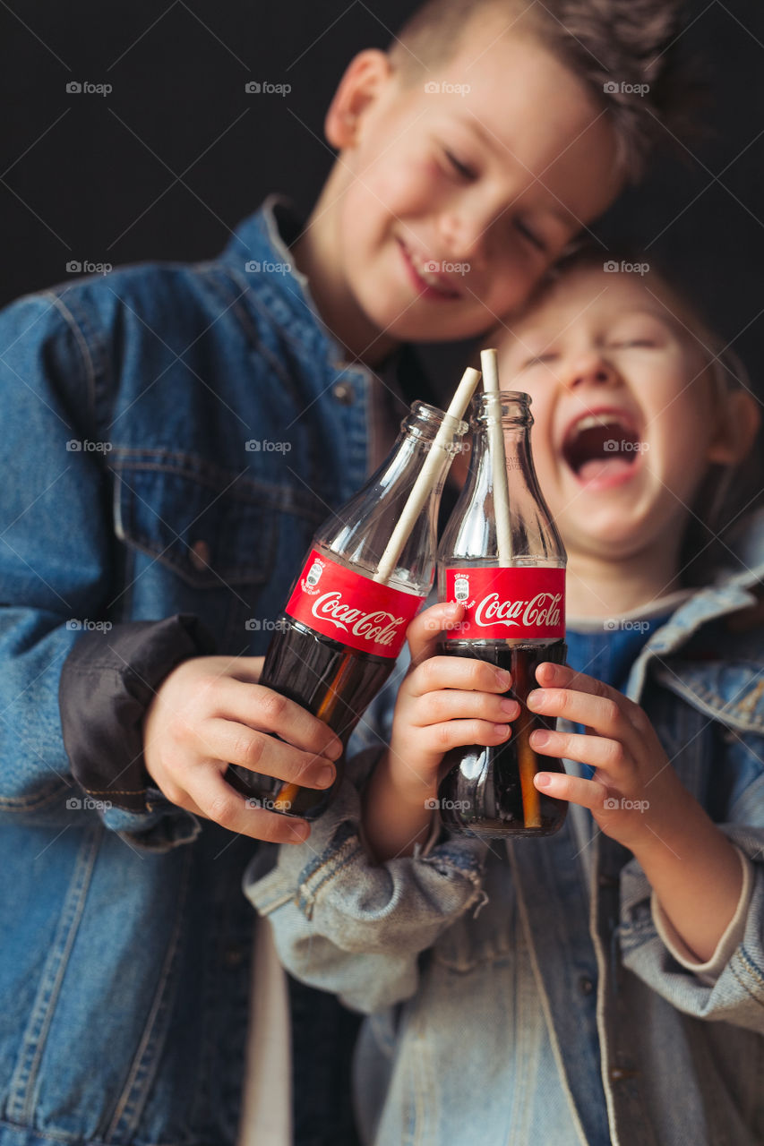 a boy and a girl of seven and five years old, friends, drinking Coca Cola, laughing, having fun, wearing denim clothes. Real emotions.lifestyle photo. Amazing kids 