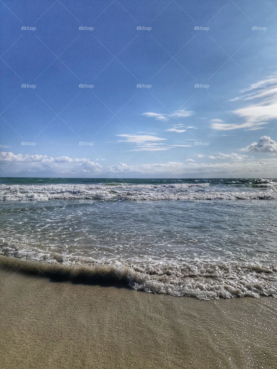 The waves are crashing on the sandy beach of Indian Rocks Beach. The sky was blue.