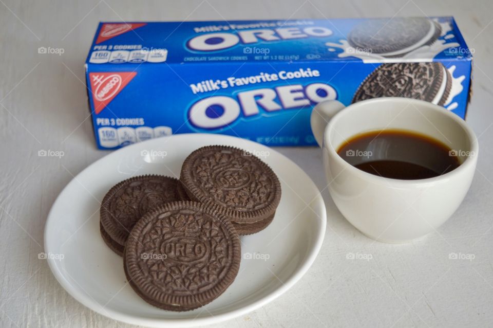 A flat lay with a pack of Oreo cookies and Oreo cookies on a white plate with a cup of coffee on a white background