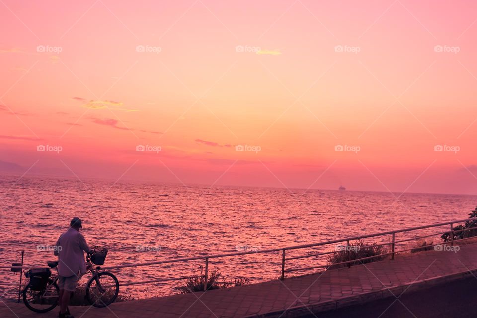 At sunset, a fisherman gathers up his fishing gear to ride his bicycle back home along the seaside promenade.