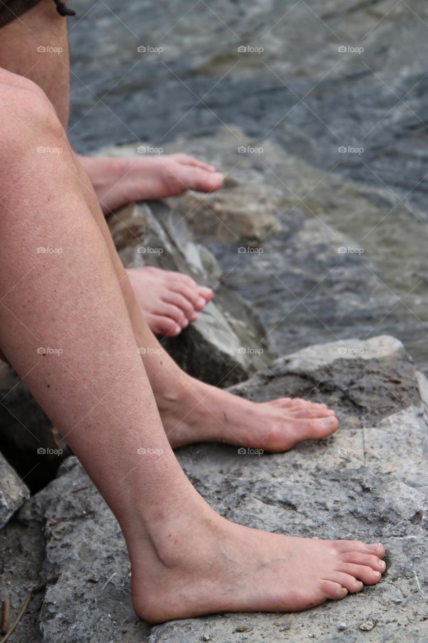 Close-up of bare feet and legs on a rock in the water