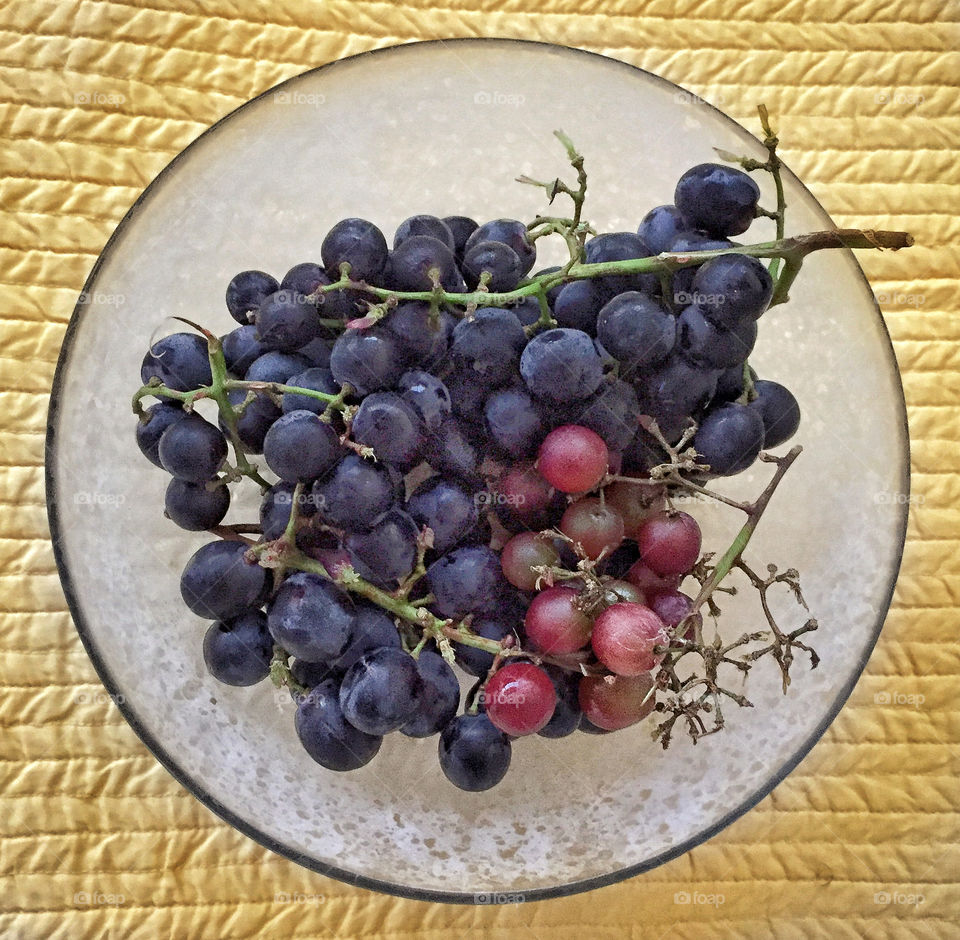 Black and red grapes in a glass bowl on a quilted yellow tablecloth 