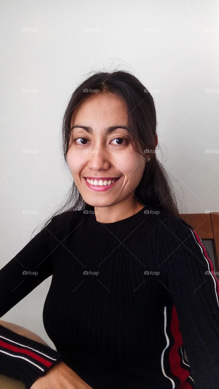 Portrait selfie of a woman smiling looking at the camera. Sitting on a brown chair.