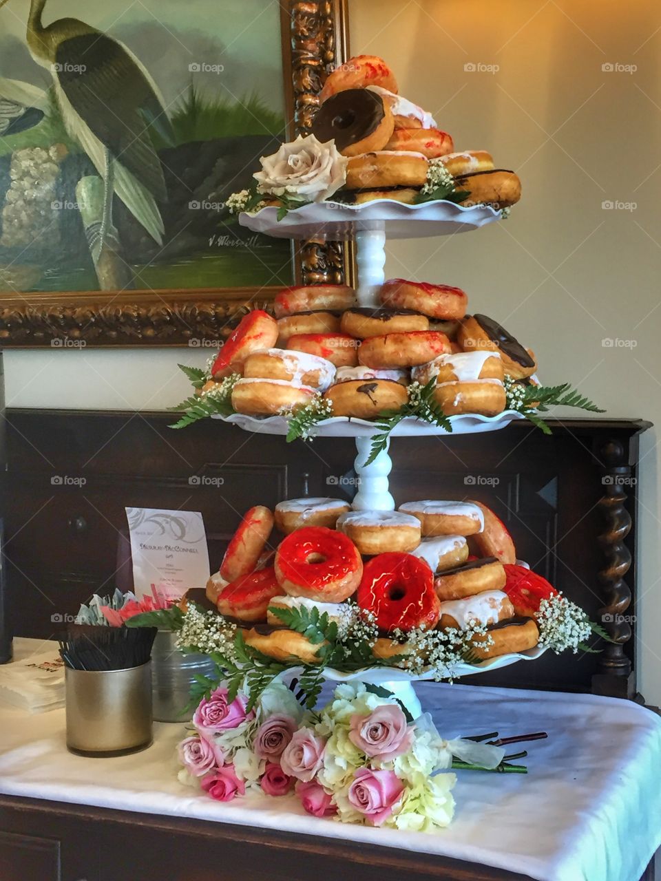 A three tiered tower of donuts on a table at a wedding reception for dessert.