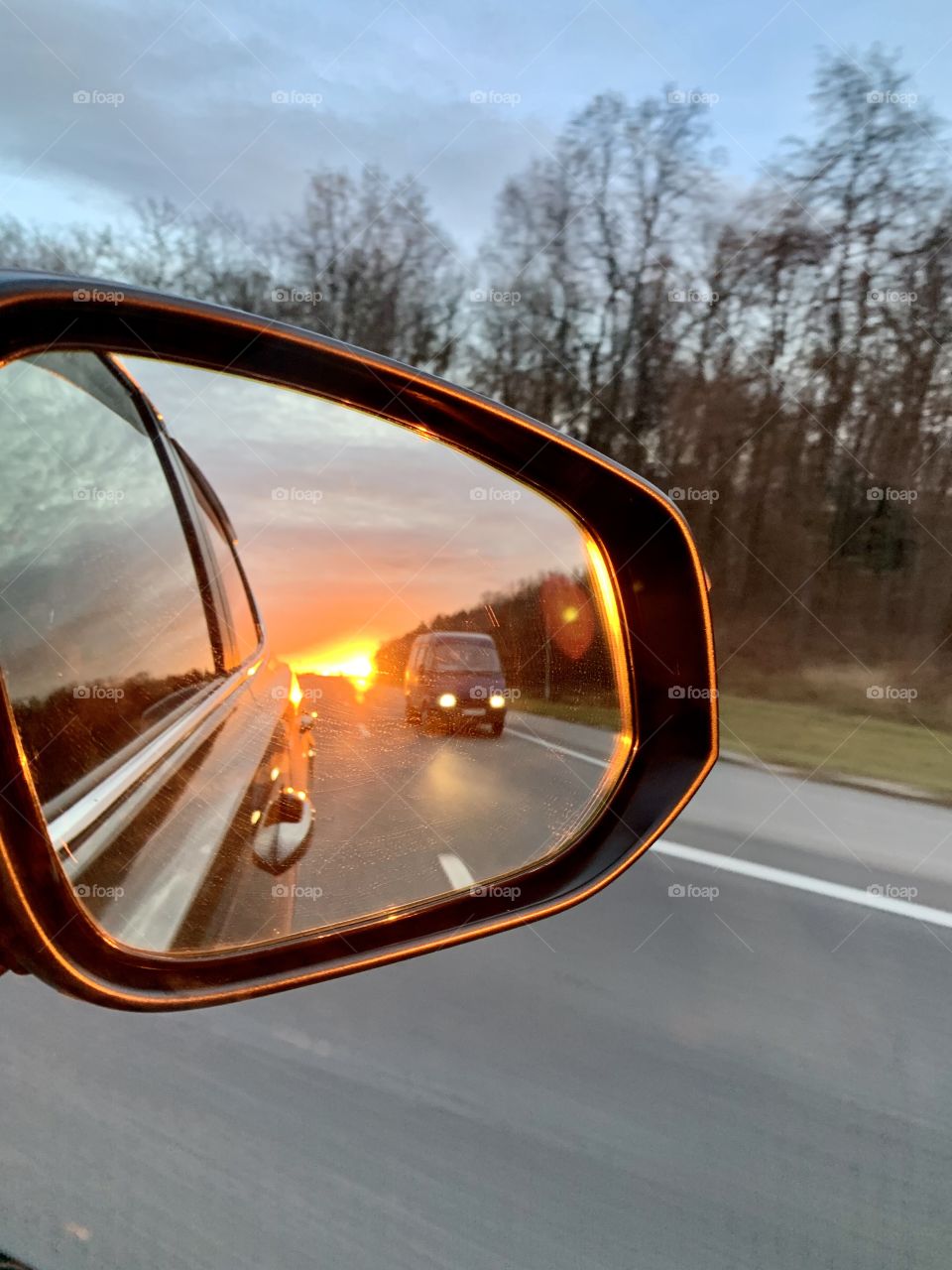 The car goes on the highway at high speed and the sunset is reflected in the side mirror