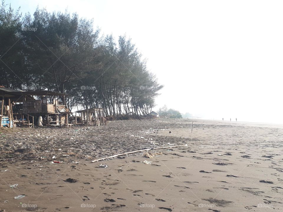 the view on the beach there are wooden houses or kiosks, strewn rubbish and trees lining the coastline in the morning looks very clear