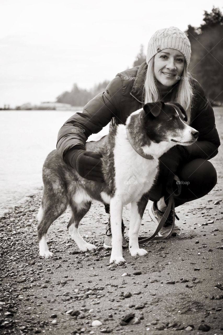 An athletic woman dressed for and her senior dog take a stroll on the beach in Washington State during winter