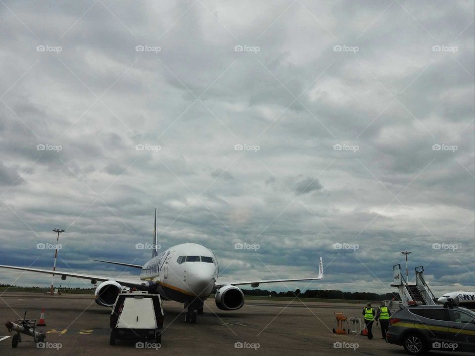 the plane at the airport with cloudy sky in the background