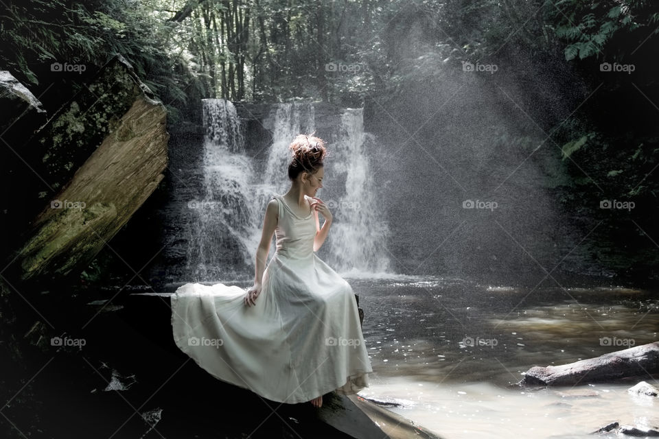 Young woman sitting on rock near waterfall