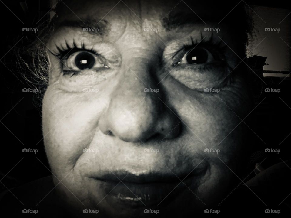 Black and white close up of a woman’s face. The angle and the severe lighting and makeup make her face look almost like a caricature and the intensity of her stare makes her look almost manic.