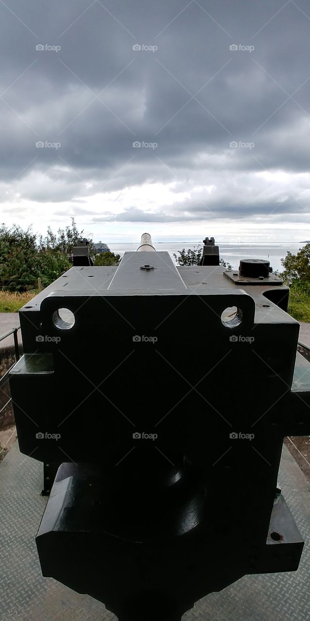 standing behind large artillery gun looking out to sea