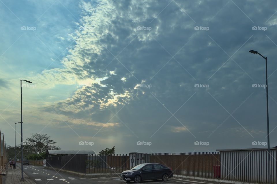 blue sky with clouds and bright sunshine illuminates a parking area with an automobile