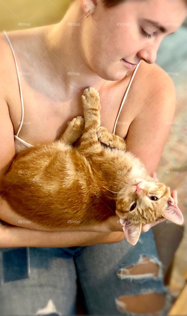 A young woman cradles a tabby kitten in her arms as the kitten relaxes in a comical pose 