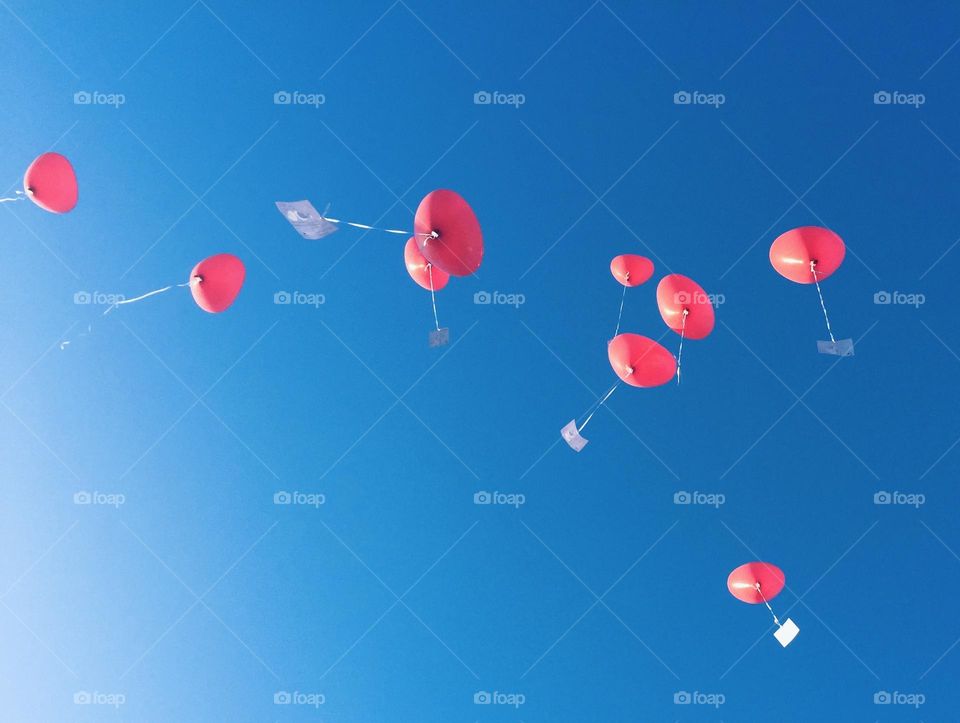 Heart-shaped helium balloons flying into the blue sky with a message attached to them.