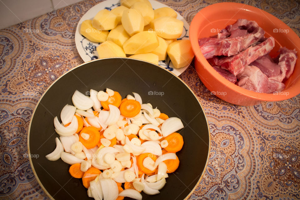 Onion, carrots, garlic, potatoes, and red meat. Ingredients for a red steak prepared in the stove on the table top view