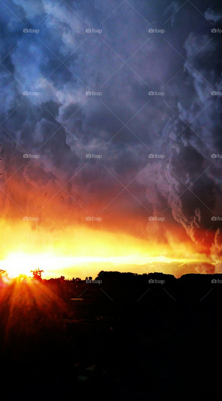 Storm clouds over silhouetted tree during sunset