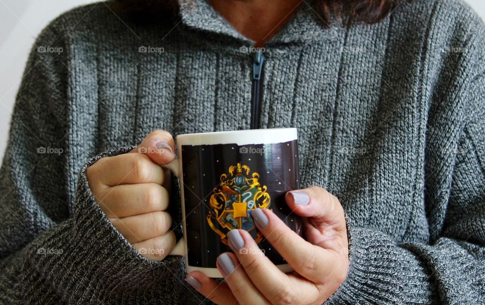 Woman wearing gray sweater holding a mug in her hands.