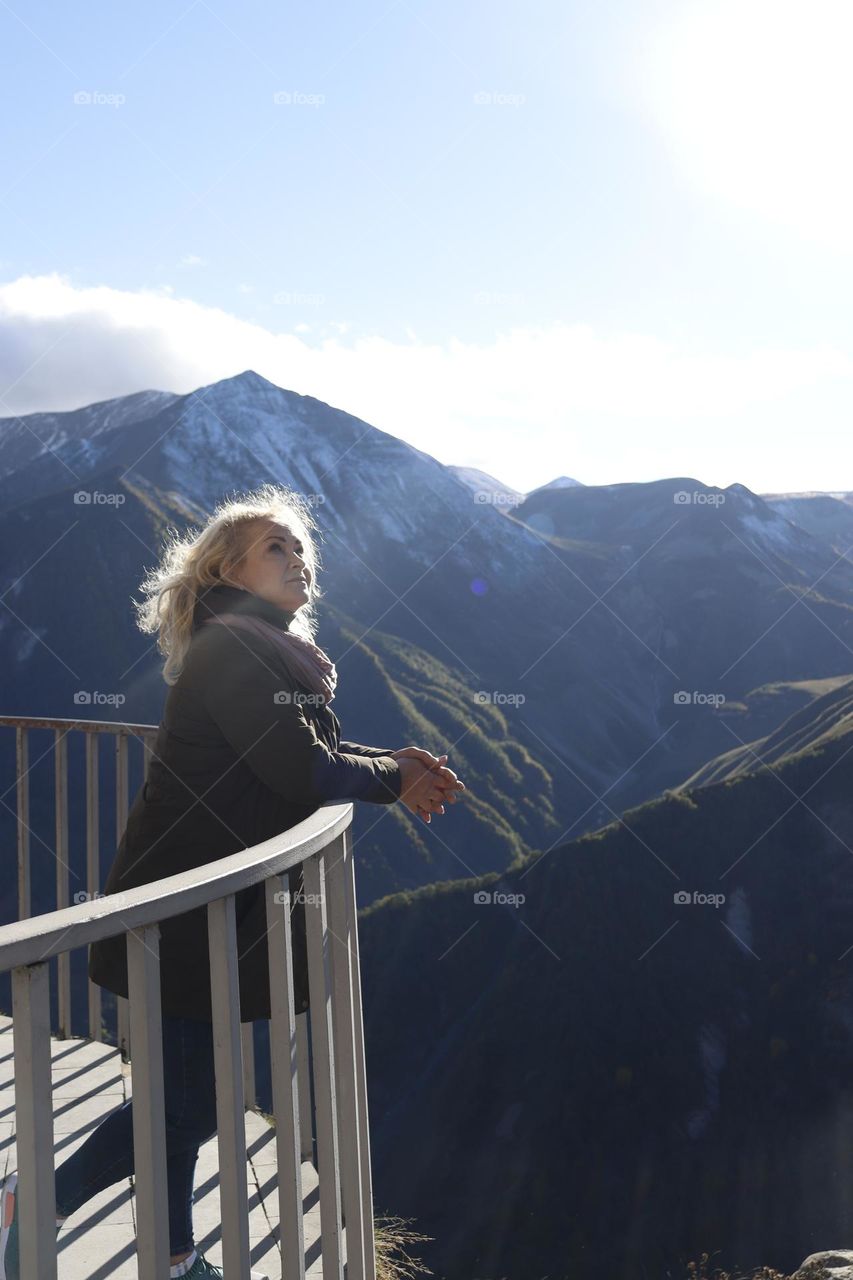 A beautiful woman looking into the sky. Majestic mountains are in the background