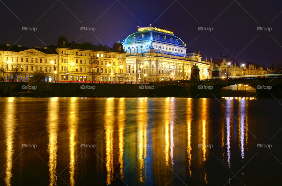 The view from the island to the National Theatre in Prague, the September night. Long glimpses of night lights and architectural lighting in the broad waters of the Vltava River