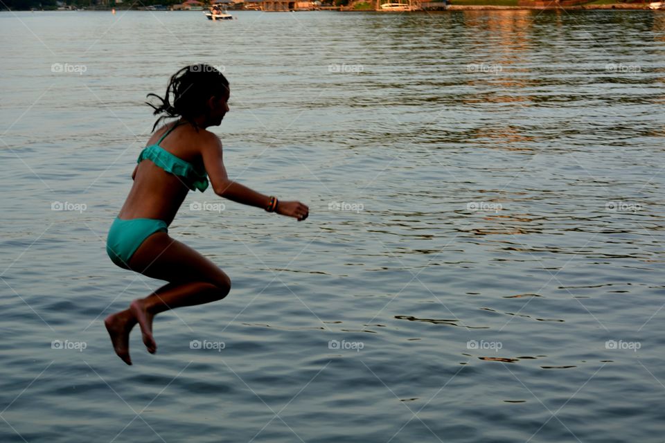 Adolescent girl jumping in to lake silhouetted against water