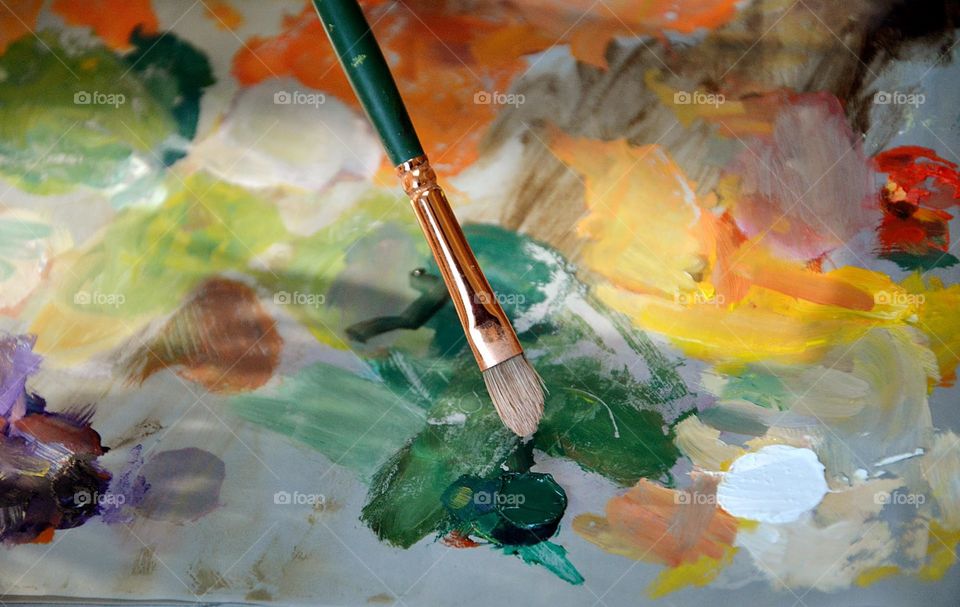 Paintbrush dipped into paint on a canvas with various colors of paint