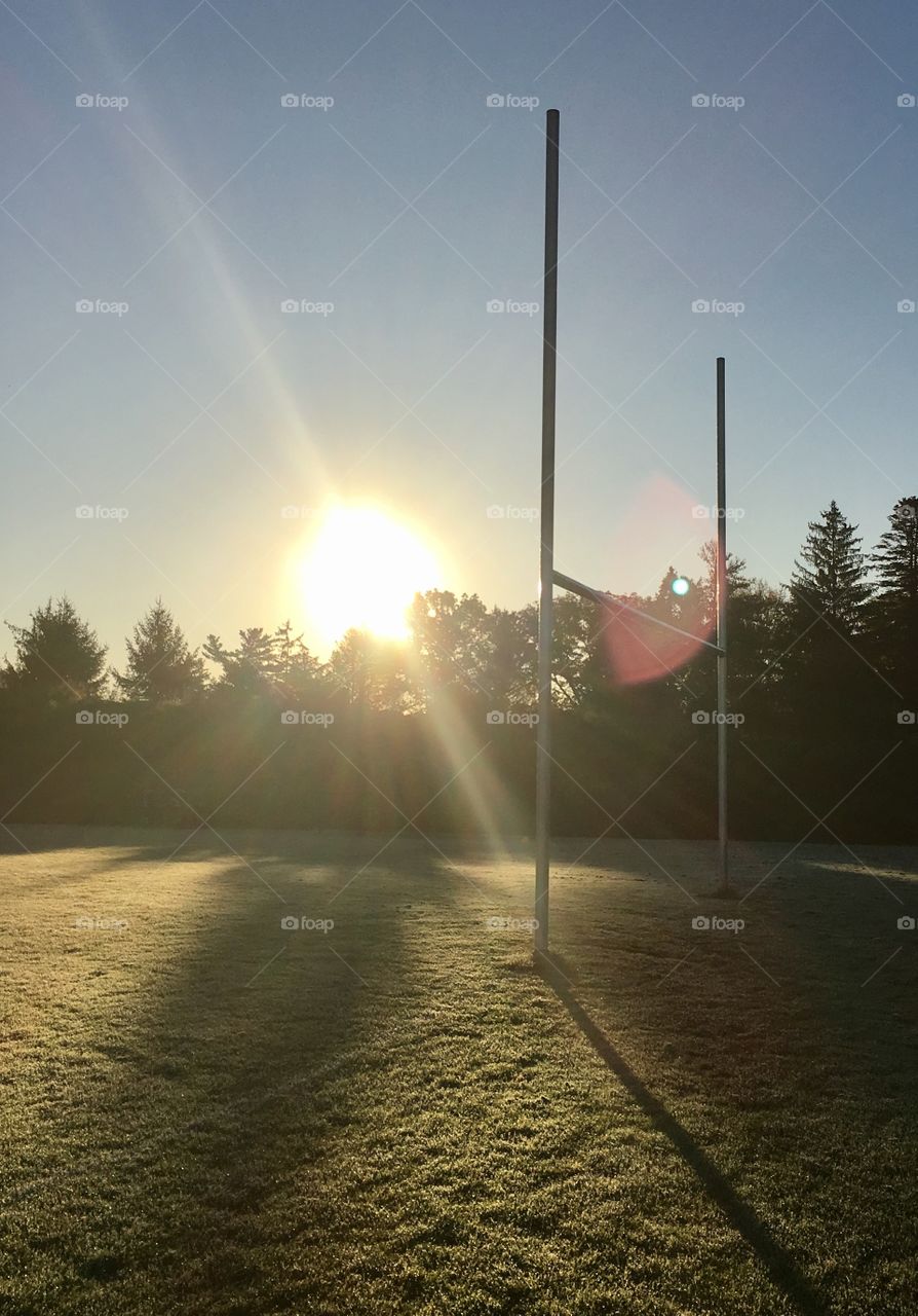 Early morning sunrise over a frost covered football field behind the goal posts