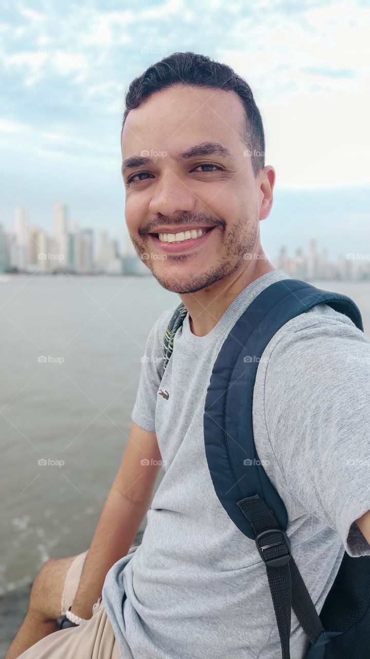 boy smiling at the camera, with city and sea in the background.
