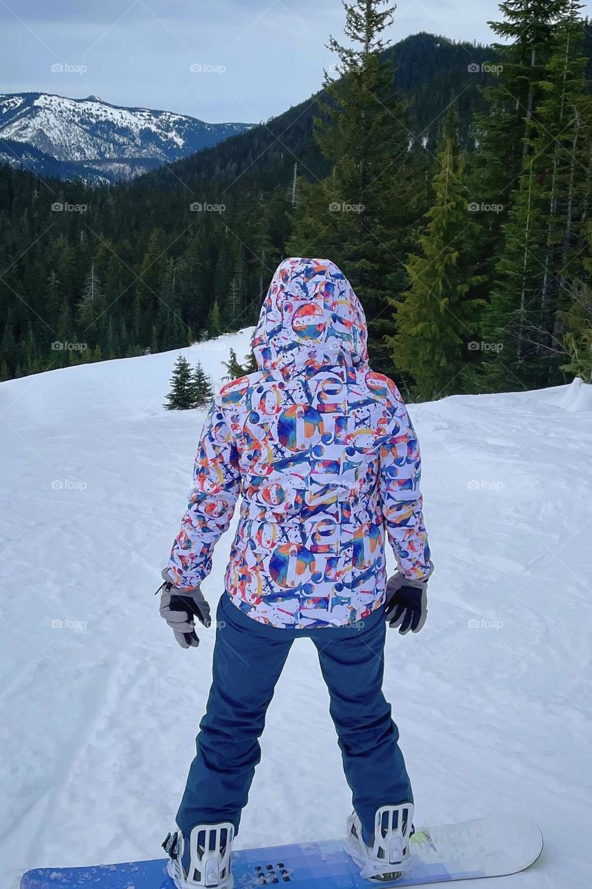 A young snowboarder checks out the snow packed run before taking a ride down the mountain 