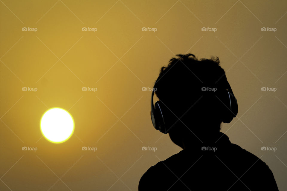 Silhouette of man with headphones on sunset sky background. Silhouette of happy man listening music.
