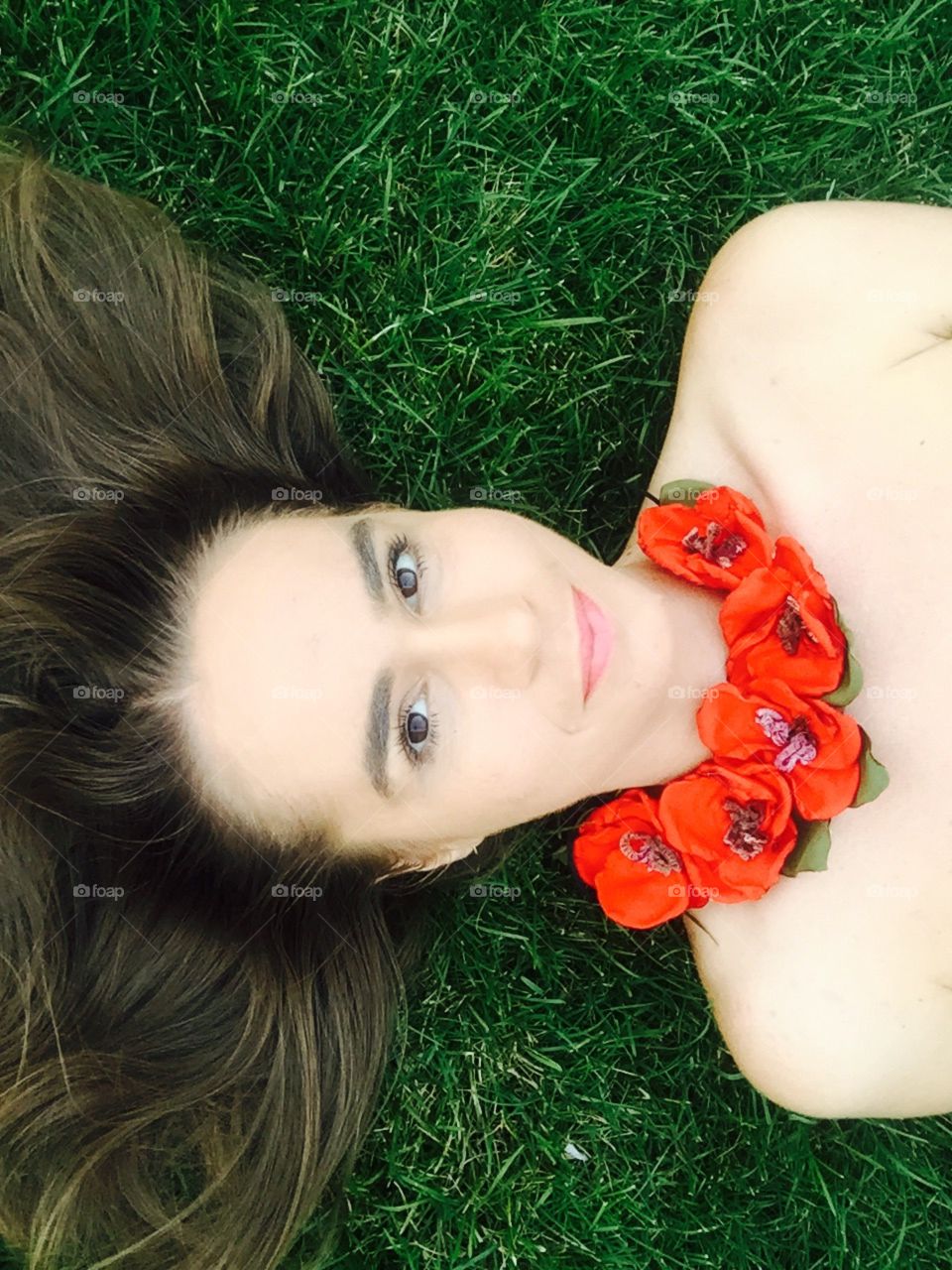 Portrait of dark blonde woman with poppies neckale laying on the grass 