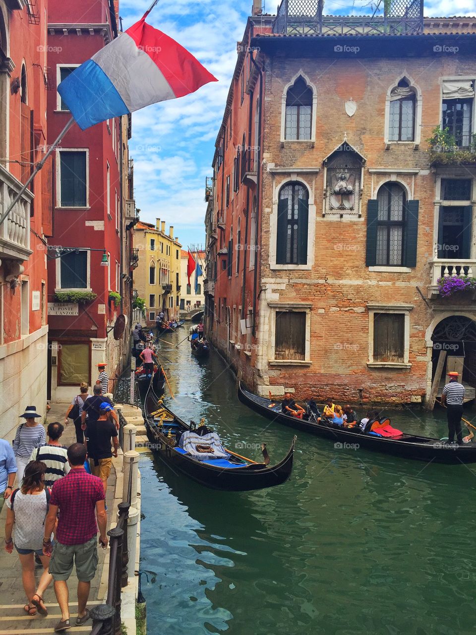 People and gondolier on canal along buildings