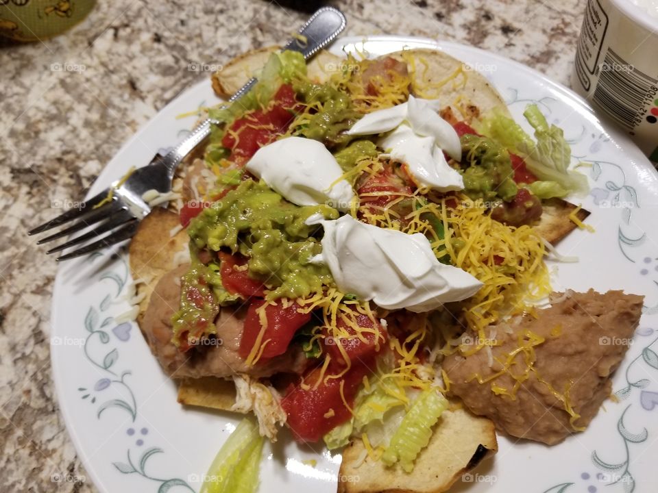 Green guacamole Mexican wrap with tomatoes, sour cream lettuce, refried beans, cheese, and put on a round plate with a silver fork.