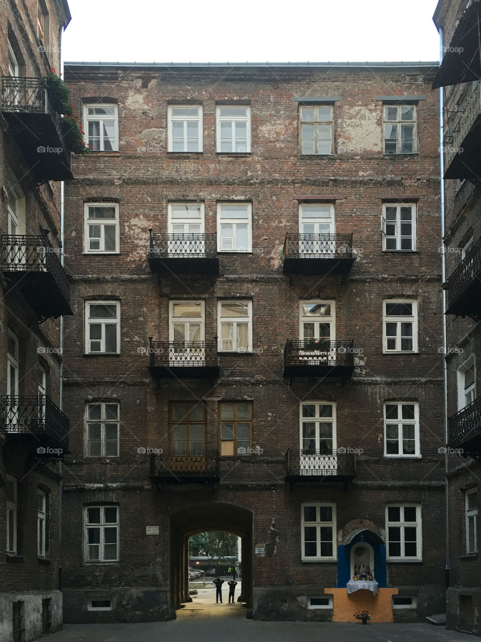 Two children playing in the backyard of old tenement house made of brick with a wallshrine on facade.